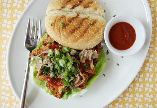 A pulled pork sandwich served on a grilled roll with homemade barbecue sauce, butter lettuce, green onions and coriander.