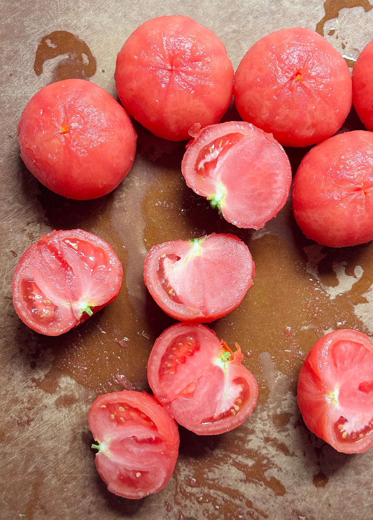 Peeled and halved tomatoes are arranged on a brown surface, with some juice and seeds visible around them. Their bright red, glossy appearance highlights their freshness—perfect for making a vibrant Fresh Tomato Sauce. // FoodNouveau.com