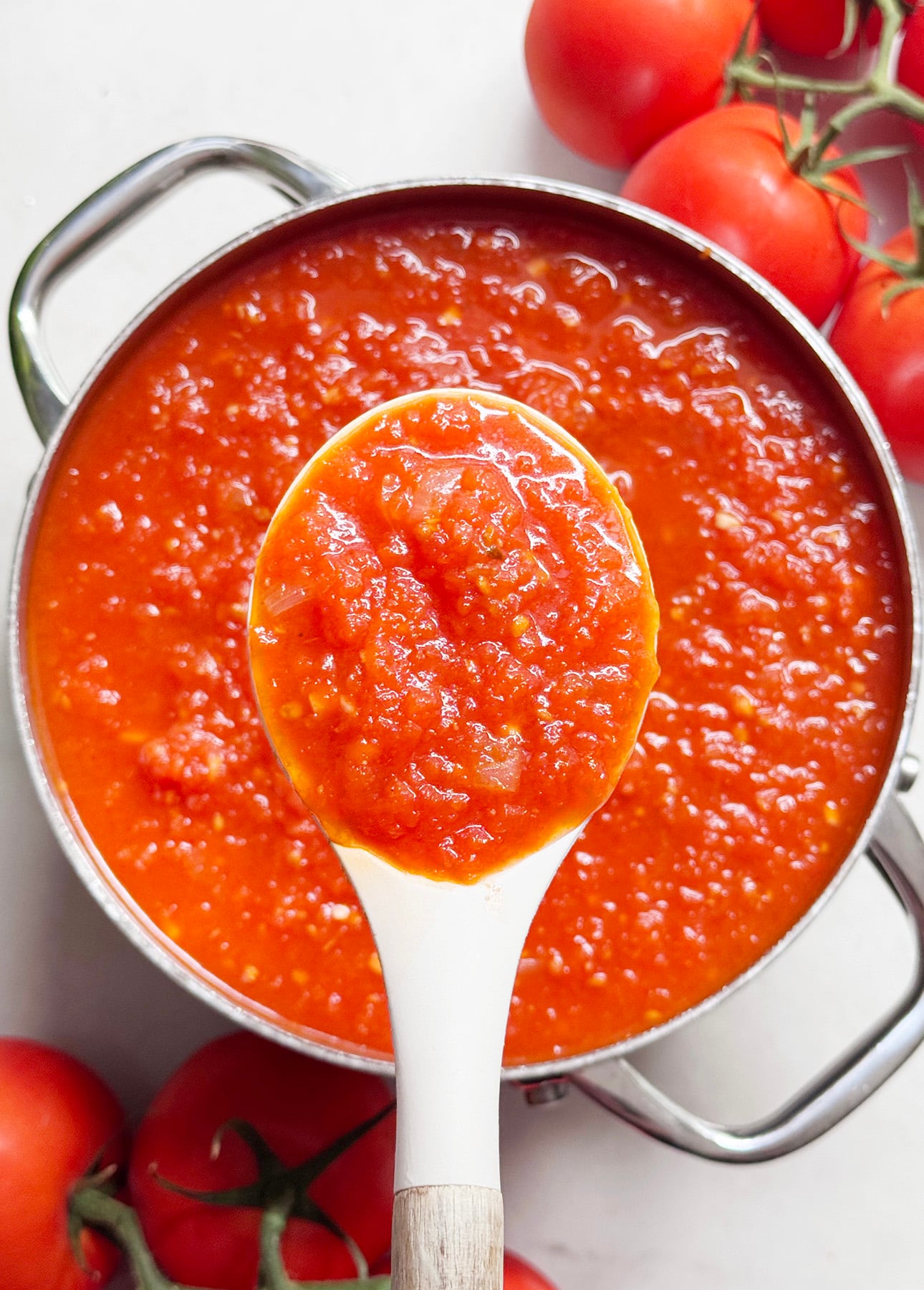 A white spoon holding chunky fresh tomato sauce above a pot filled with the same sauce, with fresh tomatoes on the vine nearby. // FoodNouveau.com