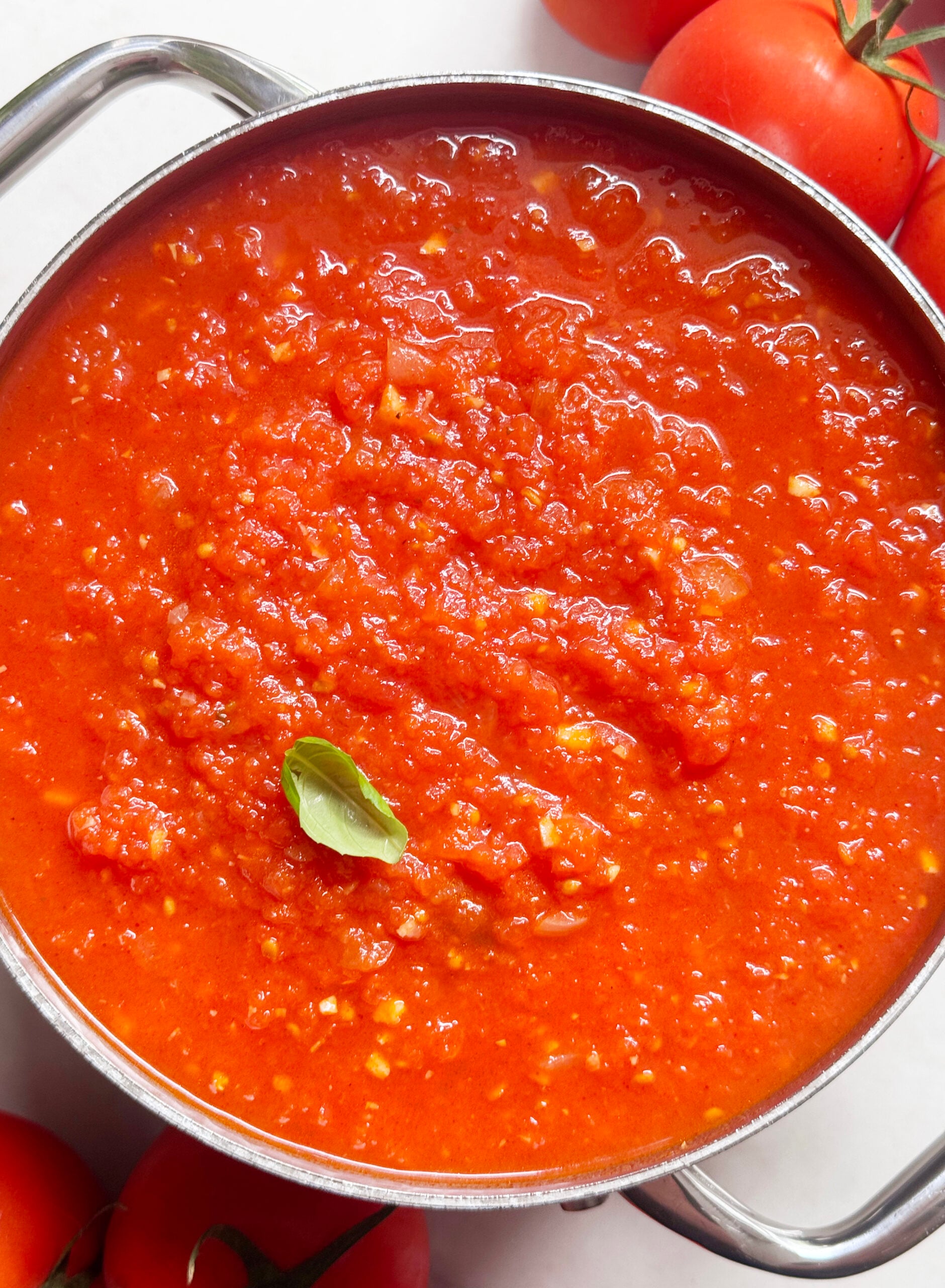 A pot of chunky fresh tomato sauce garnished with a basil leaf, surrounded by fresh tomatoes. // FoodNouveau.com
