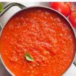 A pot of chunky Fresh Tomato Sauce garnished with a basil leaf, surrounded by ripe tomatoes. Text at the top reads, Made with any ripe tomatoes—Fresh Tomato Sauce. // FoodNouveau.com