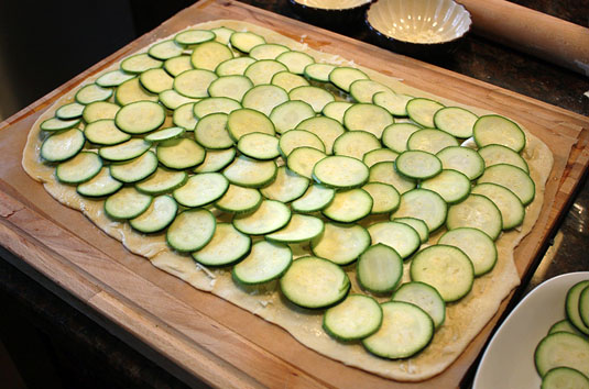 Place the thin zucchini slices over the pizza in an overlapping pattern.