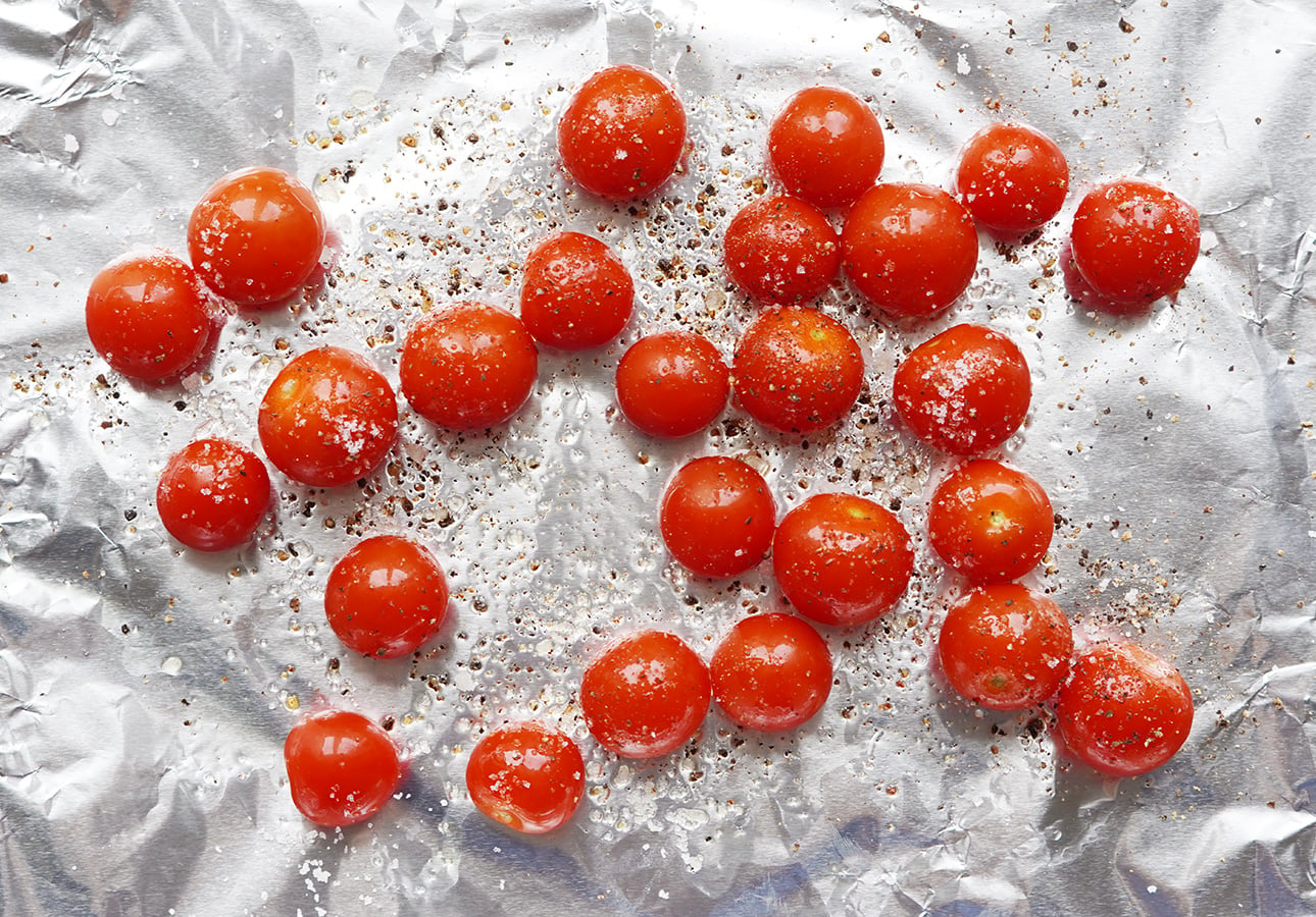 Cherry tomatoes are scattered on a sheet of aluminum foil, sprinkled with coarse salt and black pepper, ready for roasting&mdash;perfect as a topping for Roman-Style Pizza. // FoodNouveau.com