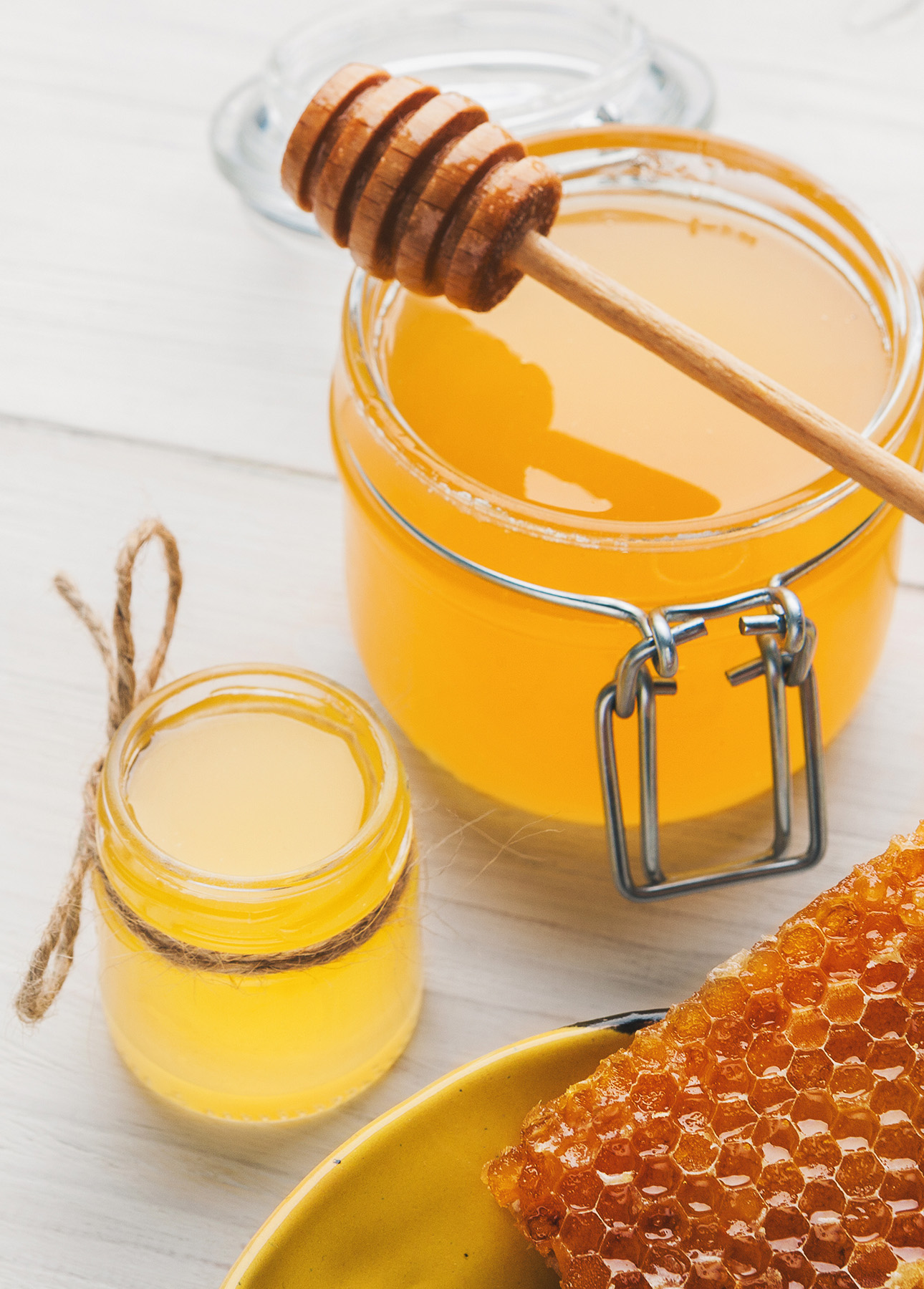 Jars of different varieties of honey along and a piece of honeycomb on a plate // FoodNouveau.com