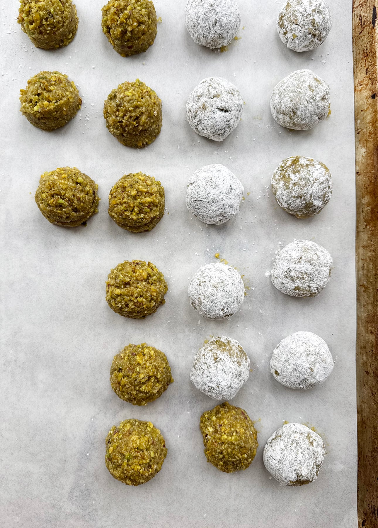 Rows of round cookie dough balls on parchment paper, with some coated in powdered sugar and others left plain, ready for baking. // FoodNouveau.com