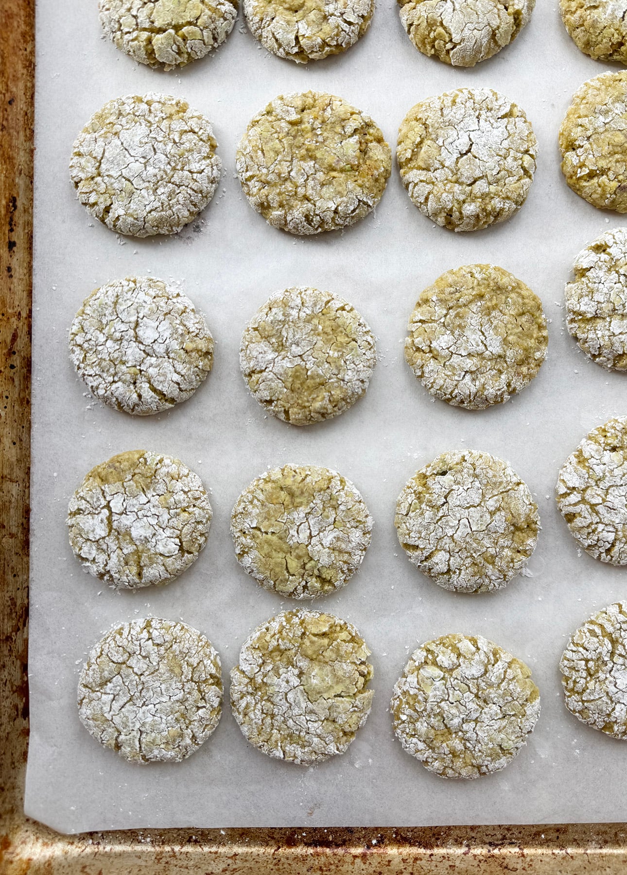 Rows of round, crinkle-topped cookies dusted with powdered sugar are arranged neatly on a sheet of parchment paper, sitting on a baking tray. The cookies appear soft and slightly golden. // FoodNouveau.com