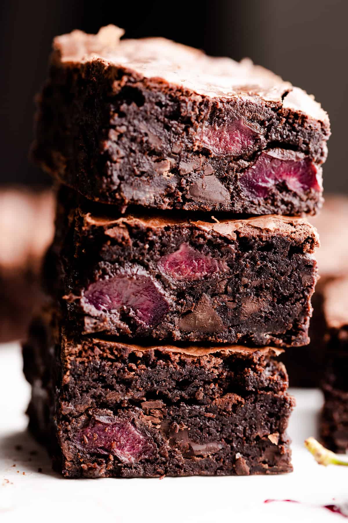 A close-up of three thick, fudgy chocolate brownies stacked on top of each other, with visible pieces of cherries inside. // FoodNouveau.com